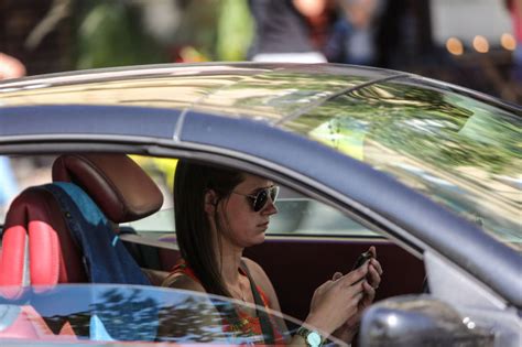 Teminė nuotrauka: žmogus, vairuojantis automobilį, su mobiliuoju telefonu, kuriame matoma „Bolt“ programėlė