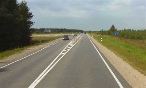 dviejų eismo juostų kelias su viduryje esančia linija, apšviestas gatvės žibintų, matomi automobiliai