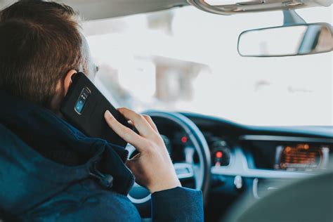 Teminė iliustracija: vairuotojas, stovintis spūstyje ir naudojantis mobiliuoju telefonu