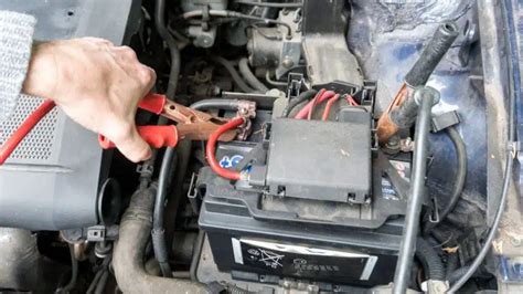 žmogus bando užvesti automobilį su laidais, prijungtais prie kito automobilio akumuliatoriaus