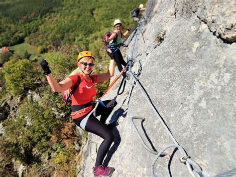 Gidas, padedantis dalyviui įveikti Via Ferrata ruožą, kalnų fone