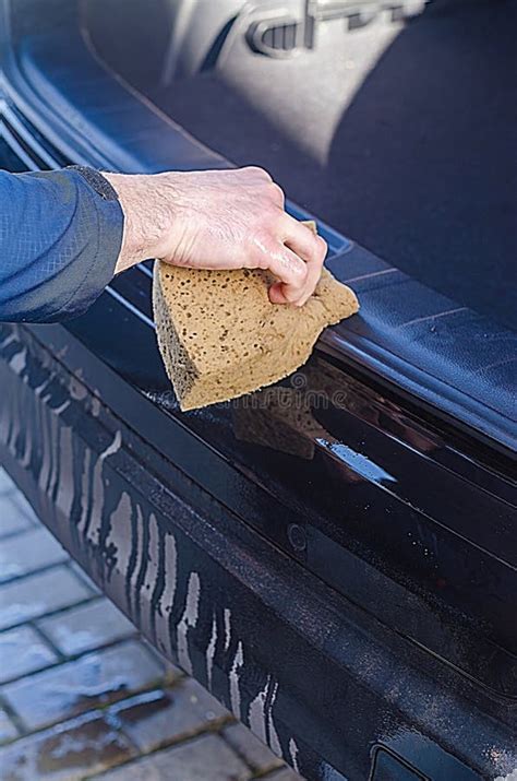 Close-up photo of someone cleaning a car door sill with a sponge and soapy water