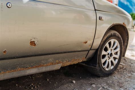 Automobilio rūdžių paveikto sparno ar kėbulo dalies detalus vaizdas su rudomis dėmėmis ir dažų pūslėmis