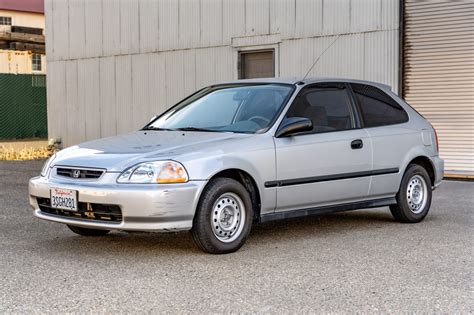 Teminis paveikslėlis: Honda Civic 1996 m. modelis, šalia automobilių dalių.