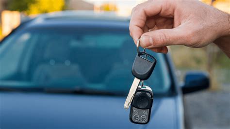 Tematinė nuotrauka: ranka laiko automobilio raktelius ir draudimo polisą, fone - automobilis ir „Regitros“ pastatas