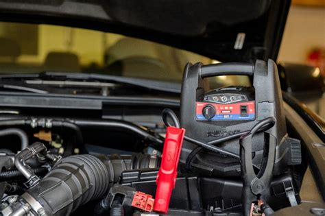 Tematinė nuotrauka: žmogus naudoja nešiojamąjį starterį (boosterį) automobilio užvedimui.