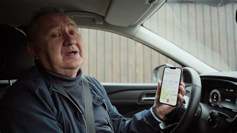 Tematinė nuotrauka: žmogus vairuojantis automobilį ir naudojantis mobiliojo telefono programėlę