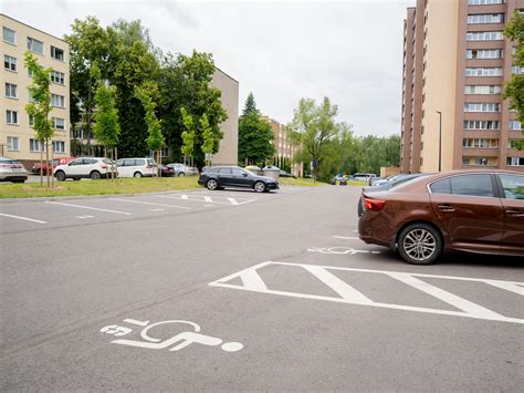 Automobilis stovintis parkavimo aikštelėje prie daugiabučio namo, atspindintis dažną nenaudojamą transporto priemonės būseną