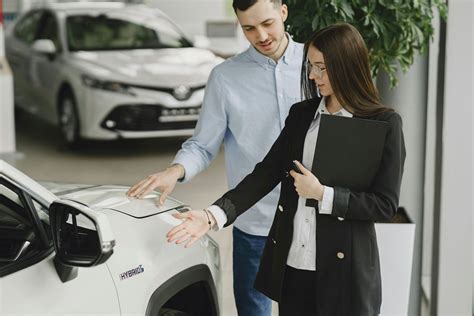 Tematinė nuotrauka: besišypsantis konsultantas ir klientas, apžiūrintis automobilį.