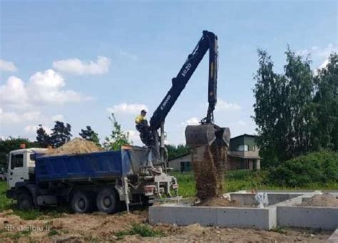Iliustracija: Krovininis sunkvežimis su integruotu hidrauliniu manipuliatoriumi, atliekantis krovinių pakrovimą