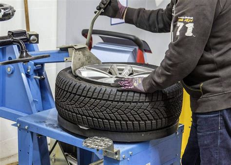 nuotrauka, vaizduojanti autoserviso specialistus, montuojančius padangas ant automobilio rato