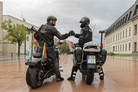 Motociklininkas su šalmu ir keleivis, dėvintis šalmą, sėdi ant motociklo.