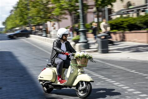Jaunuolis su šalmu sėdi ant mopedo mieste