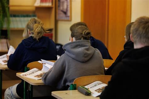 Teorijos pamoka vairavimo mokykloje, šviesi klasė, mokiniai prie stalų, dėstytojas rodo skaidres