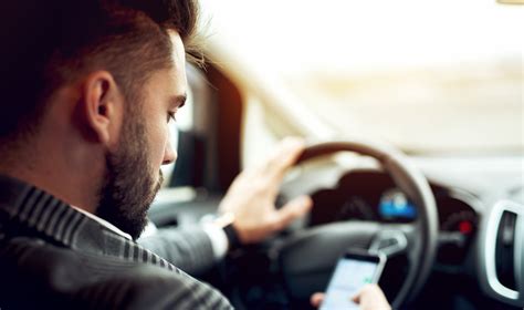 Tematinė nuotrauka: žmogus prie vairo, užsakinėjantis paslaugą išmaniuoju telefonu