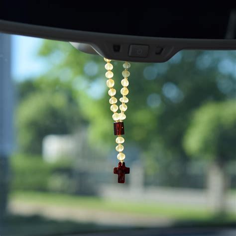 nuotrauka, kurioje rožančius elegantiškai pakabintas ant automobilio galinio vaizdo veidrodėlio