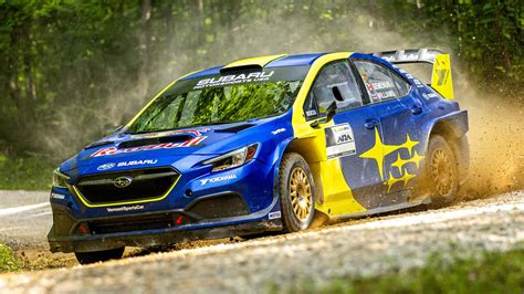 The iconic blue Subaru WRX STI rally car speeding on a dirt track, with dust flying