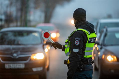 Teminis nuotraukos paveikslėlis, kuriame pavaizduotas policijos automobilis stabdantis automobilį už KET pažeidimą, su fone matomais kelio ženklais.