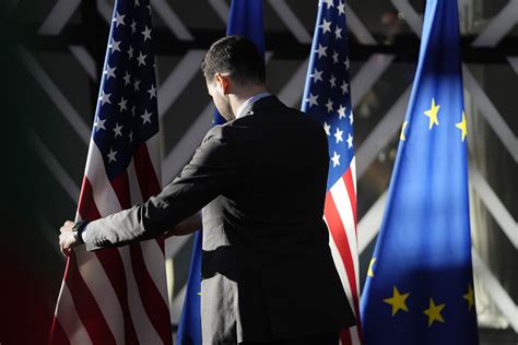 Tematinė nuotrauka, vaizduojanti JAV ir ES vėliavas, susijusias su prekybos susitarimais, ir amerikietiškus automobilius